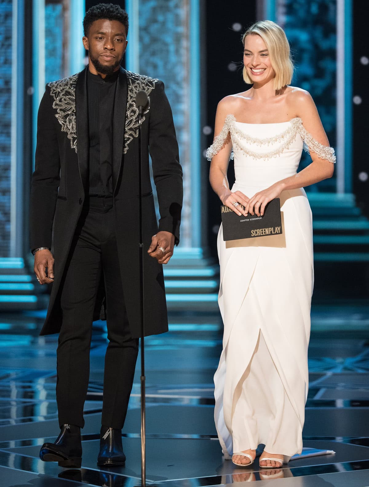 Chadwick Boseman and Margot Robbie present the Oscar for Best Adapted Screenplay during the 90th Academy Awards at the Dolby Theatre in Hollywood, California, on March 4, 2018, with Robbie wearing a custom Chanel Haute Couture gown by Karl Lagerfeld, white satin Roger Vivier 'Es'sensual' sandals, Chanel Fine Jewelry, and a matching Chanel clutch