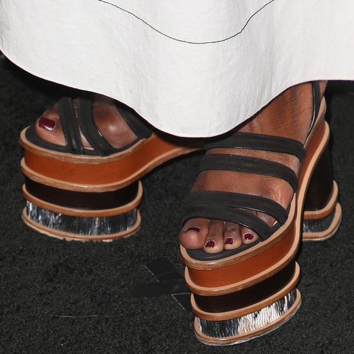 Danai Gurira's shoes feature black leather straps, a sculptural wooden sole, and eye-catching metallic accents