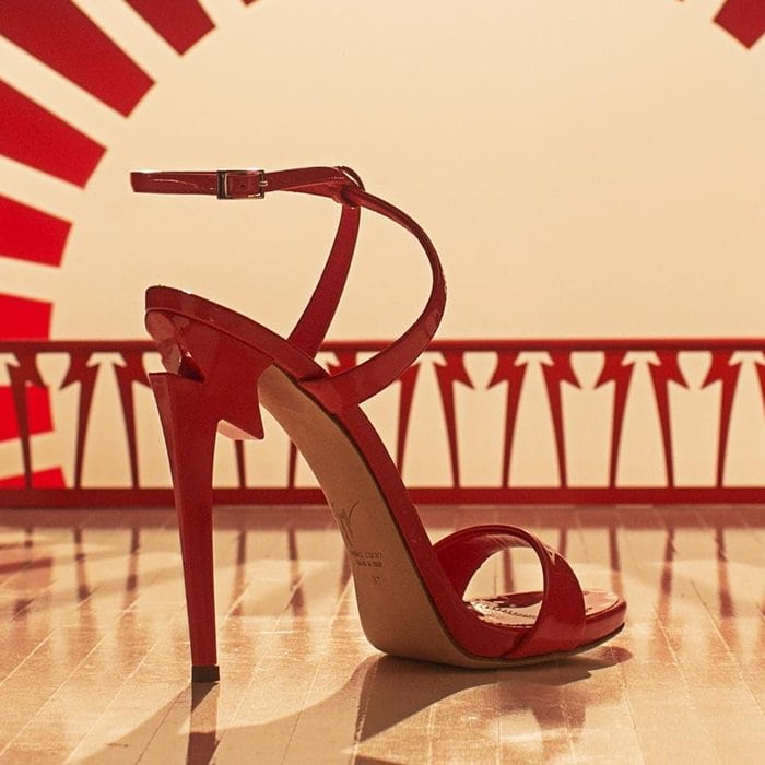 A red patent pair is spotlighted in a studio setting, where the clean lines and lightning-shaped heel take center stage