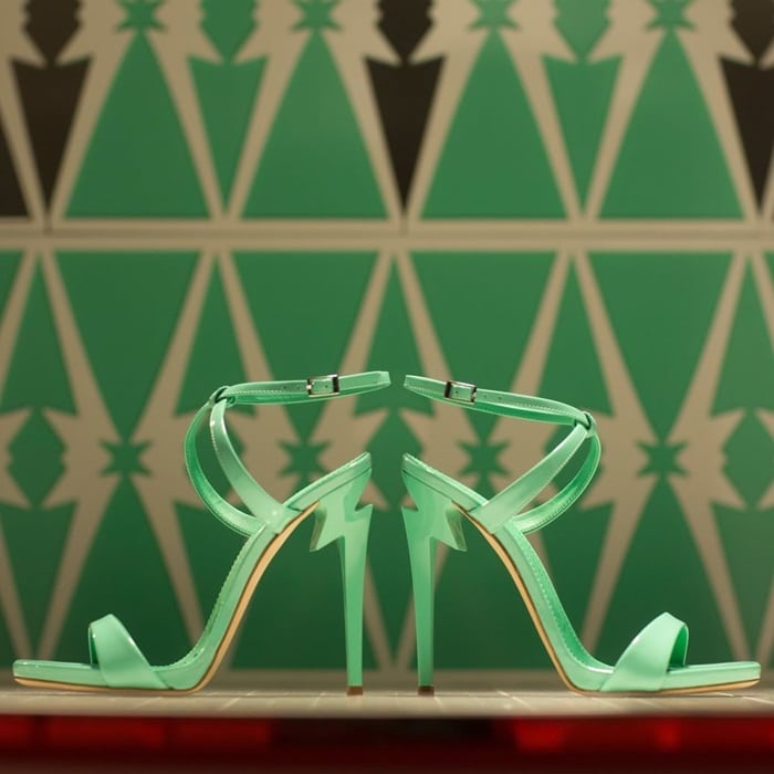 Mint green “G Heel” sandals are displayed in a mirrored presentation, highlighting the sleek ankle strap and the sculptural heel’s architectural silhouette