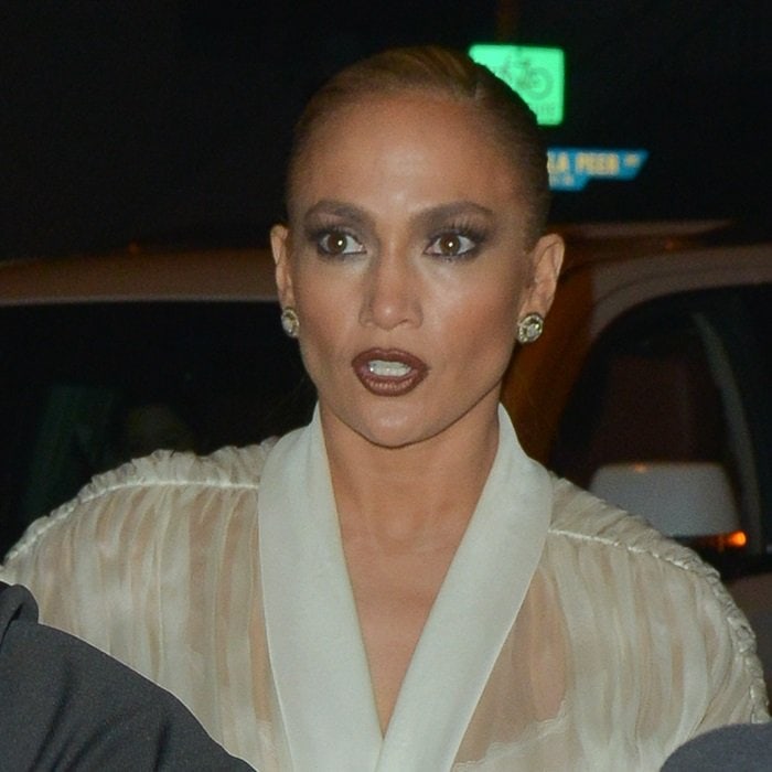 Jennifer Lopez’s dramatic smoky eye and slicked-back ponytail sharpen the contrast between her sheer Ashish blouse and the casual denim foundation of the look