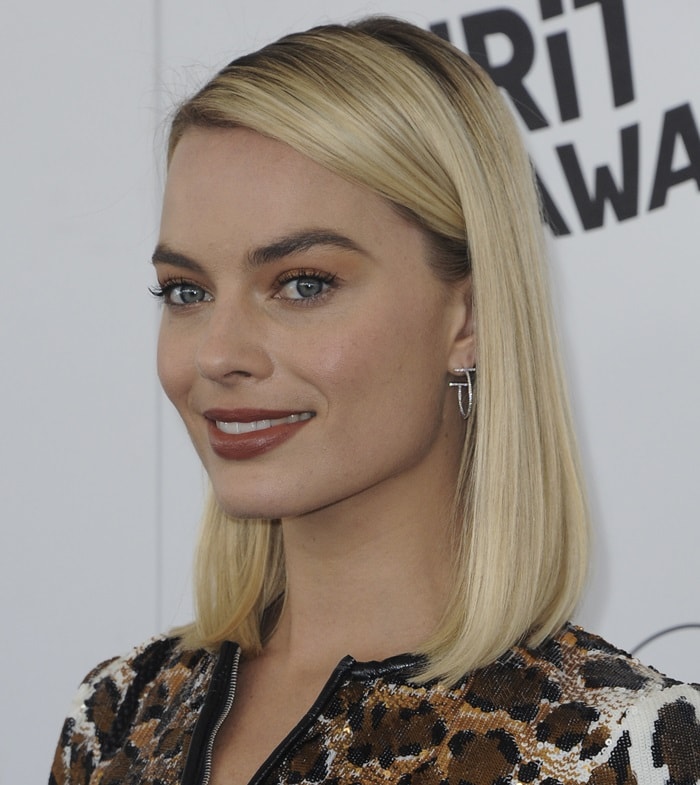 Margot Robbie keeps her beauty look clean and understated, pairing a sleek blonde bob with Tiffany T earrings and soft neutral makeup