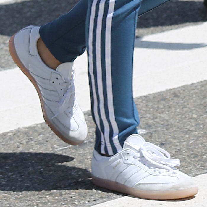A close-up view of Emily Ratajkowski's white Adidas Samba sneakers, paired with blue Adidas track pants