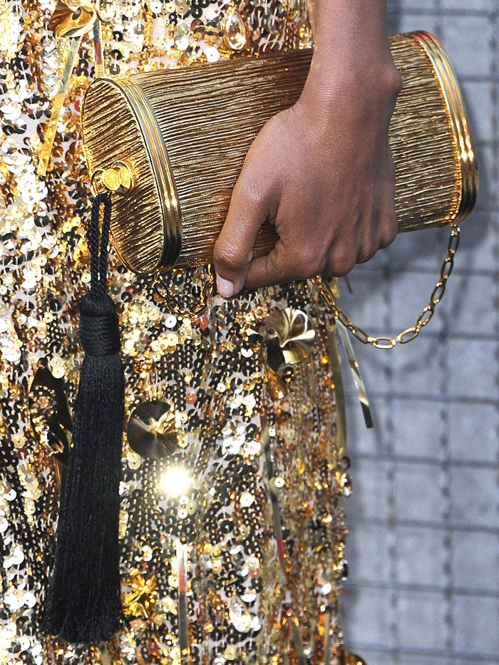 Details of Naomie Harris' Bienen-Davis gold tube clutch with black tassel detail.