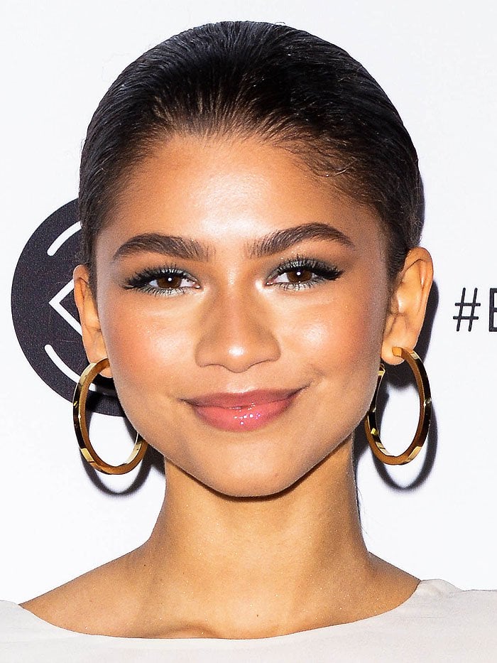 Zendaya at Beautycon 2018, wearing Jennifer Fisher “Erin” gold hoop earrings that added a bold, modern edge to her sleek braided hairstyle and art-inspired ensemble