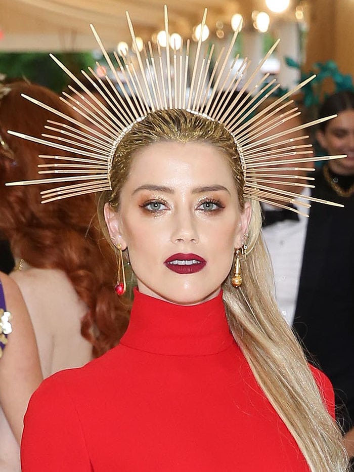 Amber Heard radiates power in a sleek red Carolina Herrera gown, crowned with a dramatic zip-tie halo by Apatico and accented with bold berry lips and mismatched drop earrings