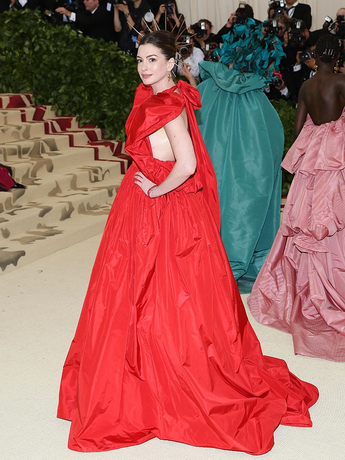 Anne Hathaway wearing a Valentino Spring 2018 Couture ruffled halter ball gown, James Banks earrings, a The Code bracelet, a gold spiked halo, and Jimmy Choo heels at the 2018 Met Gala