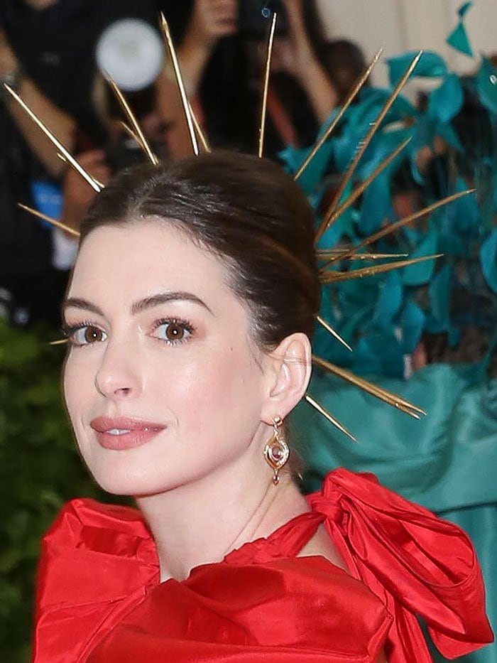 Anne Hathaway exudes celestial drama in a bold red Valentino gown, elevated by a striking gold spiked halo and sculptural detailing at the neckline
