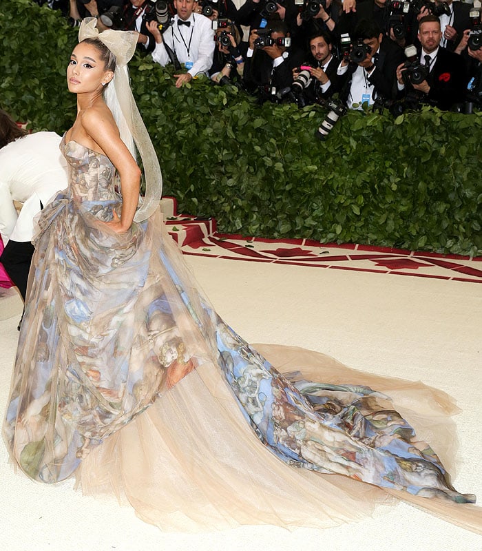 Ariana Grande turns the 2018 Met Gala staircase into a Renaissance tableau in a custom Vera Wang ball gown printed with imagery from Michelangelo’s The Last Judgment, finished with a dramatic sweeping train