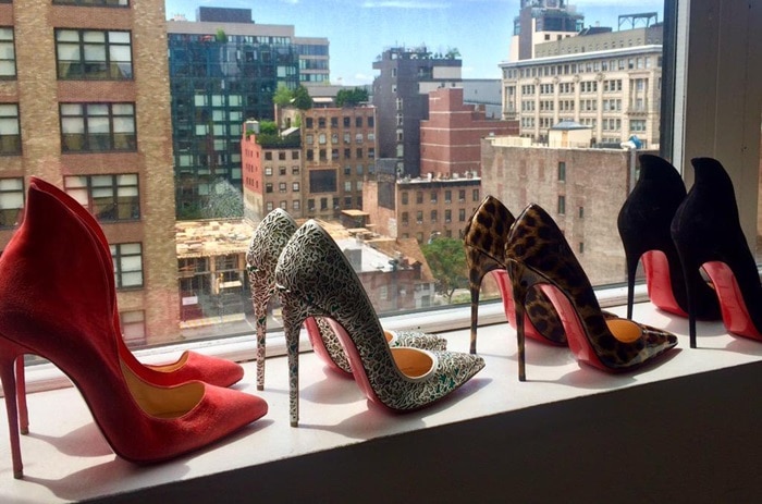 A vibrant lineup of Christian Louboutin heels displayed against a city skyline, featuring the iconic 'Mea Culpa,' 'So Pretty,' and 'So Kate' designs, each showcasing the signature red sole and exquisite craftsmanship