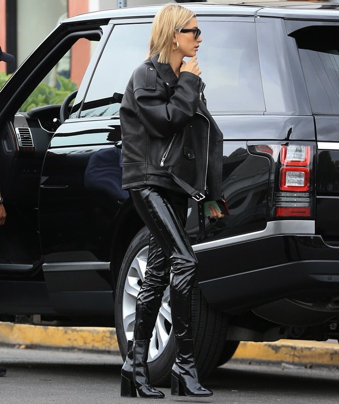 Hailey Baldwin channels edgy off-duty style in a Paul Joe Paris Bogdanov leather jacket and RTA Madison vinyl pants, finishing the sleek monochrome look with black Ash “Feel” patent leather boots and Celine Edge sunglasses