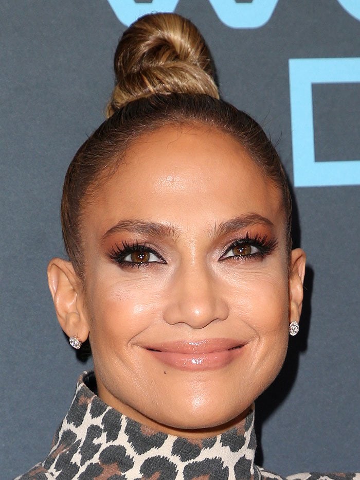 Jennifer Lopez showcases a sleek top-knot hairstyle paired with soft, glamorous makeup and sparkling diamond stud earrings