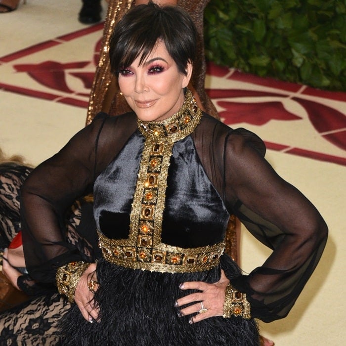 Kris Jenner in a black long-sleeve gown featuring gold and burgundy jeweled embellishments and a feather-embellished skirt