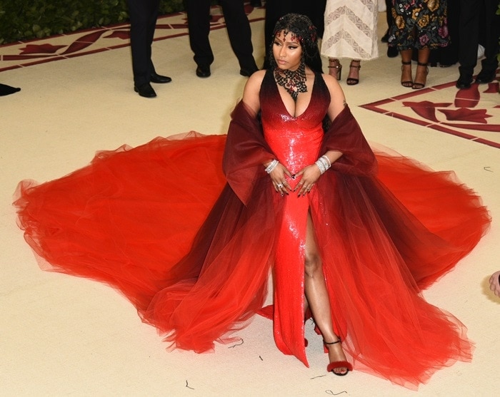 Nicki Minaj in a custom Oscar de la Renta ombré-red sequined gown, dip-dyed tulle coat, a black-and-red rosary headpiece, and Le Silla "Gaga" red-fur sandals at the 2018 Met Gala