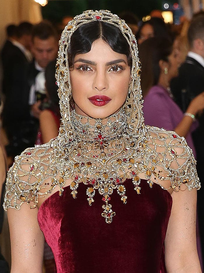 Priyanka Chopra captivates in a rich burgundy velvet gown by Ralph Lauren, elevated by an ornate, jewel-encrusted hood that evokes divine elegance and old-world regality