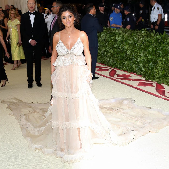 Selena Gomez in a custom Coach vintage-silk-gauze crystal-embellished slip gown with a long train and custom Coach silver C-link-embellished ankle-strap sandals at the 2018 Met Gala held at the Metropolitan Museum of Art in New York City on May 7, 2018