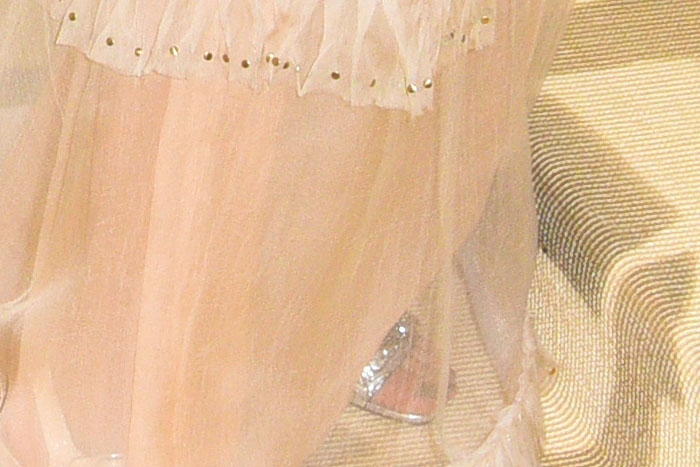 A close-up of Selena Gomez's custom Coach sandals, featuring silver C-link embellishments on the toe straps visible through her silk-gauze gown