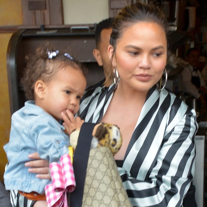 Chrissy Teigen carries daughter Luna while balancing bold black-and-white stripes with oversized hoop earrings and a relaxed, off-duty polish