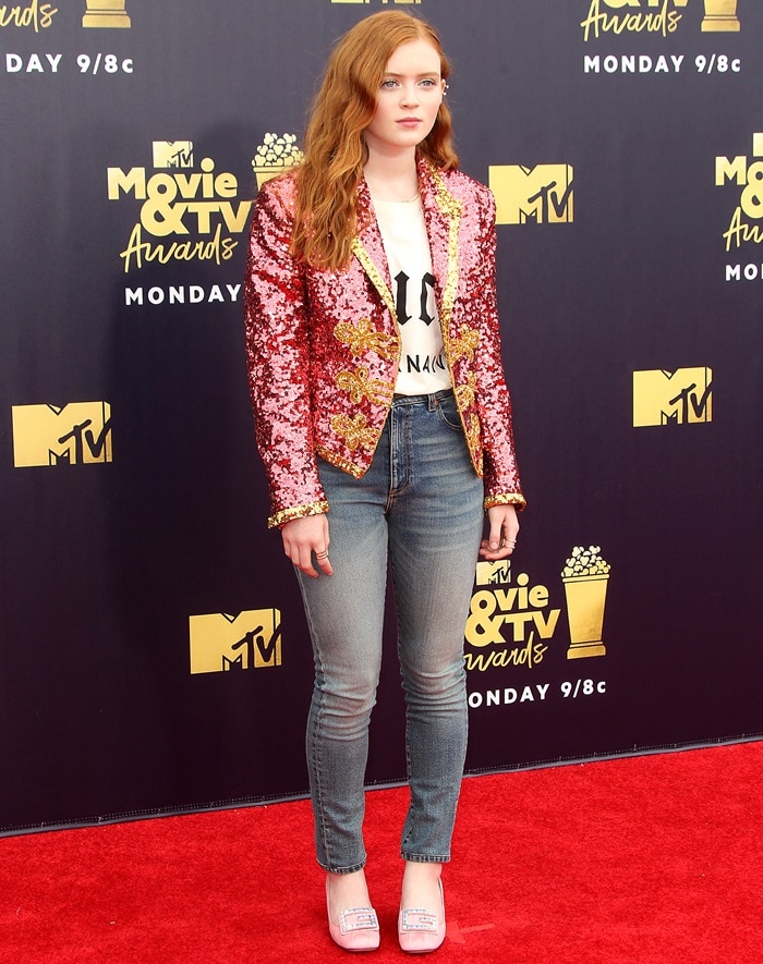 Sadie Sink rocks a bold yet youthful look, pairing a sequined pink Gucci jacket with classic skinny jeans and light pink silk moiré pumps, creating a perfect mix of glam and casual