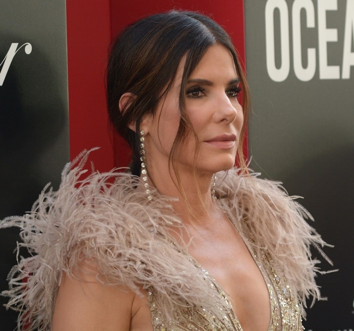 Sandra Bullock paired soft face-framing tendrils with dramatic feathered shoulders and cascading diamond earrings at the New York premiere of Ocean’s 8
