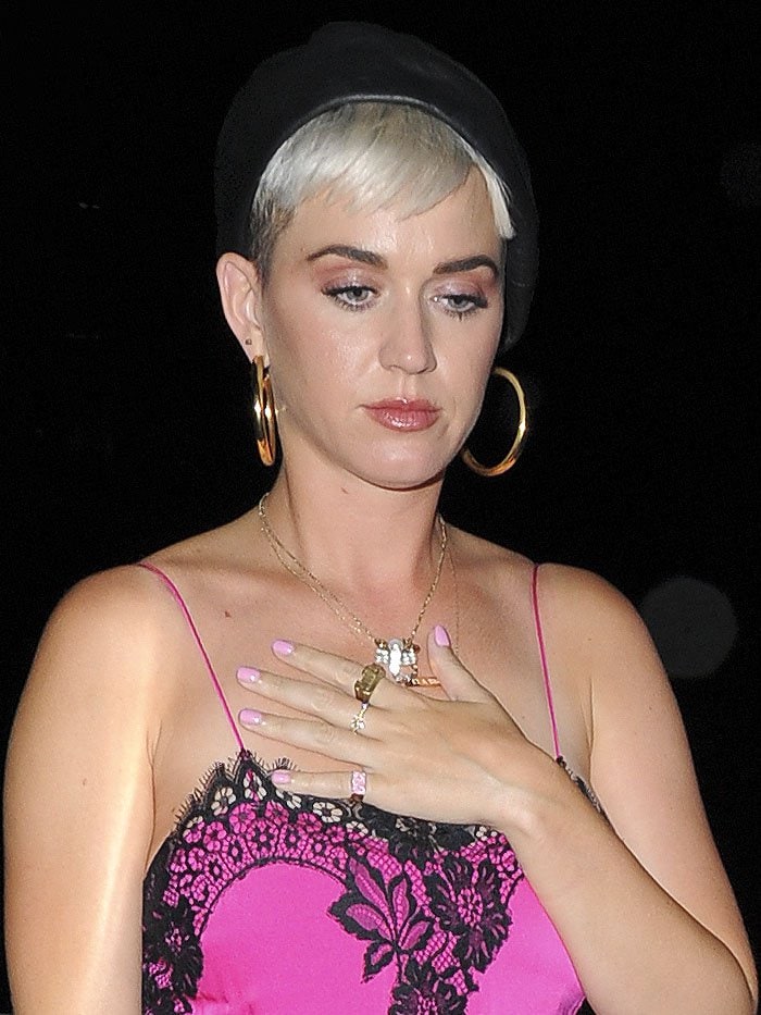 Katy Perry wearing a scorpion necklace, gold hoop earrings, and a black beret.