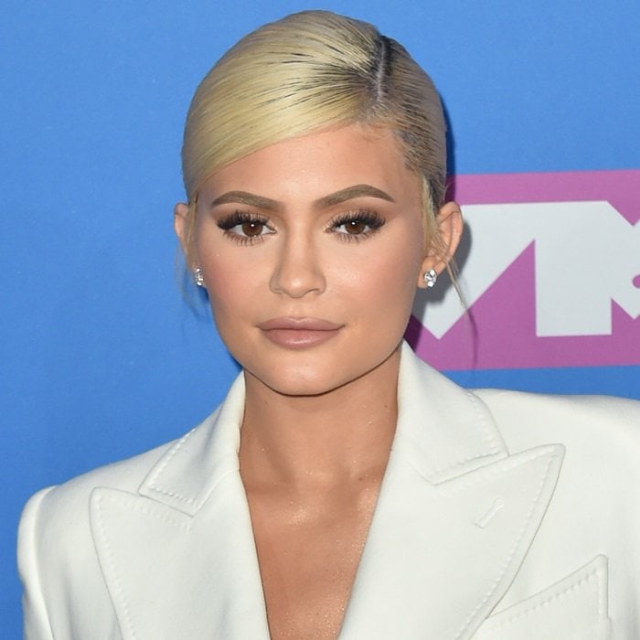 Kylie Jenner’s sleek platinum-blonde updo and softly contoured makeup deliver a polished, modern beauty look that complements her tailored ensemble