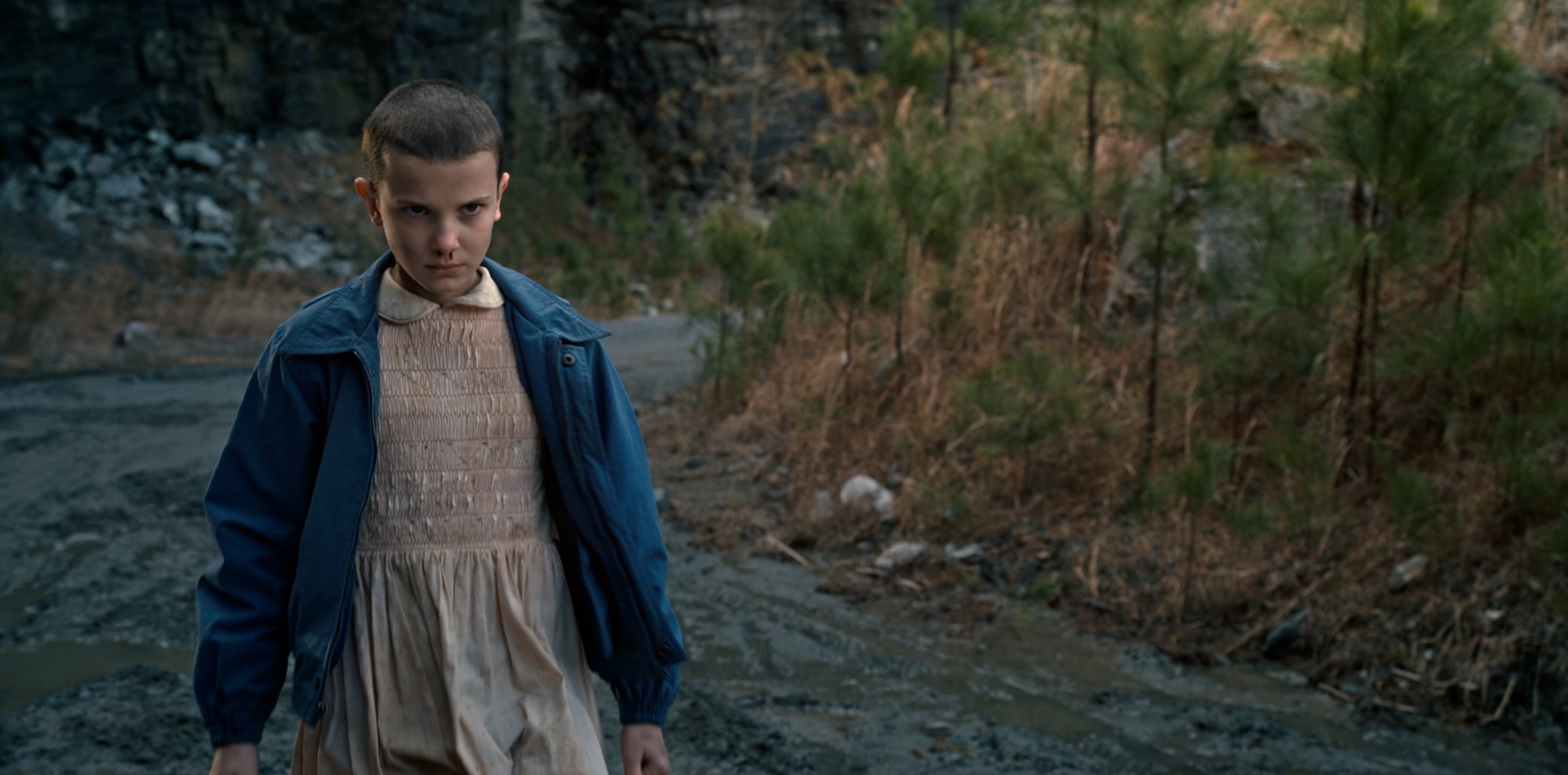 Millie Bobby Brown transforms into Eleven in Stranger Things Season 1, wearing her now-iconic pink dress and blue jacket during one of the show's most intense early scenes