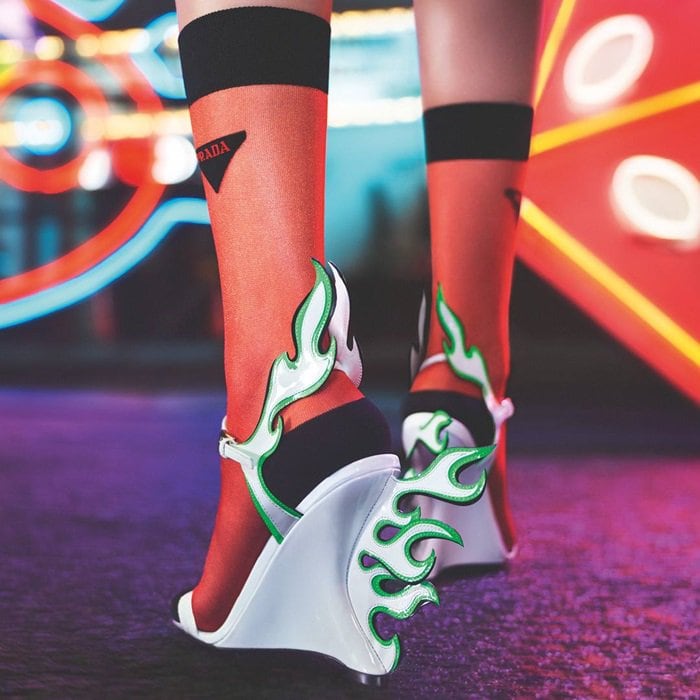 Prada’s Fall 2018 Flame wedges paired fluorescent green laser-cut patent leather flames with sculptural white wedges and sheer logo socks, reimagining the brand’s iconic hot-rod-inspired shoe motif through a futuristic cyber-neon lens