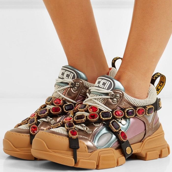 Gucci’s Flashtrek sneakers spotlight the house’s maximalist aesthetic, combining a chunky hiking-boot sole with metallic leather panels and signature crystal-wrapped straps for a bold, fashion-forward finish