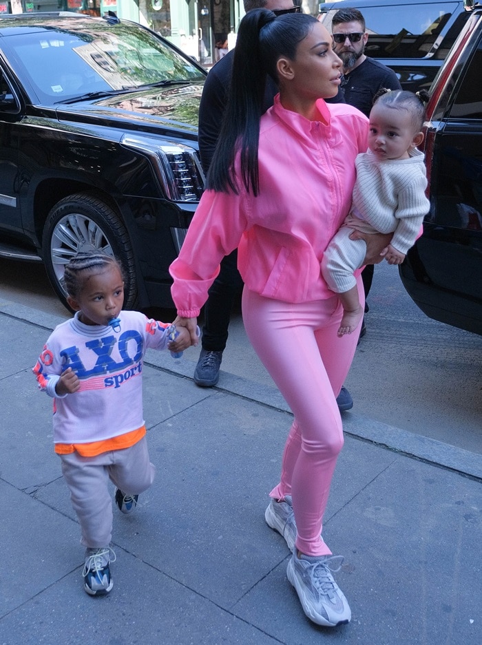 Kim Kardashian balances her monochrome pink street-style look with gray Yeezy sneakers while carrying Chicago and walking with Saint in New York City