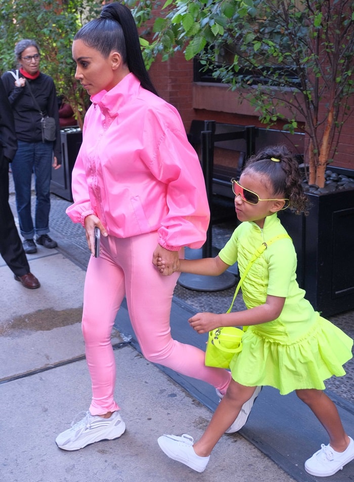 Kim Kardashian pairs second-skin pink Balenciaga pants with chunky gray Yeezy Boost 700 V2 “Static” sneakers, while North West adds a neon-green counterpoint in sporty white sneakers