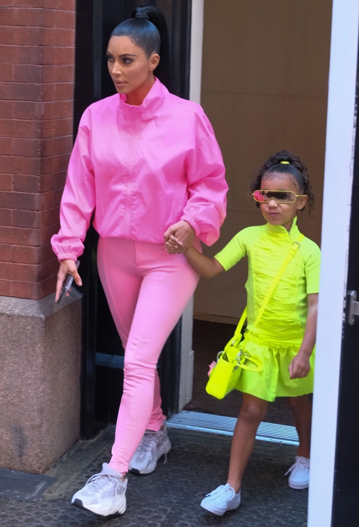 Kim Kardashian steps out in New York City in a bubblegum-pink zip jacket, matching Balenciaga stretch-satin skinny pants, and chunky gray Yeezy sneakers while holding North West’s hand