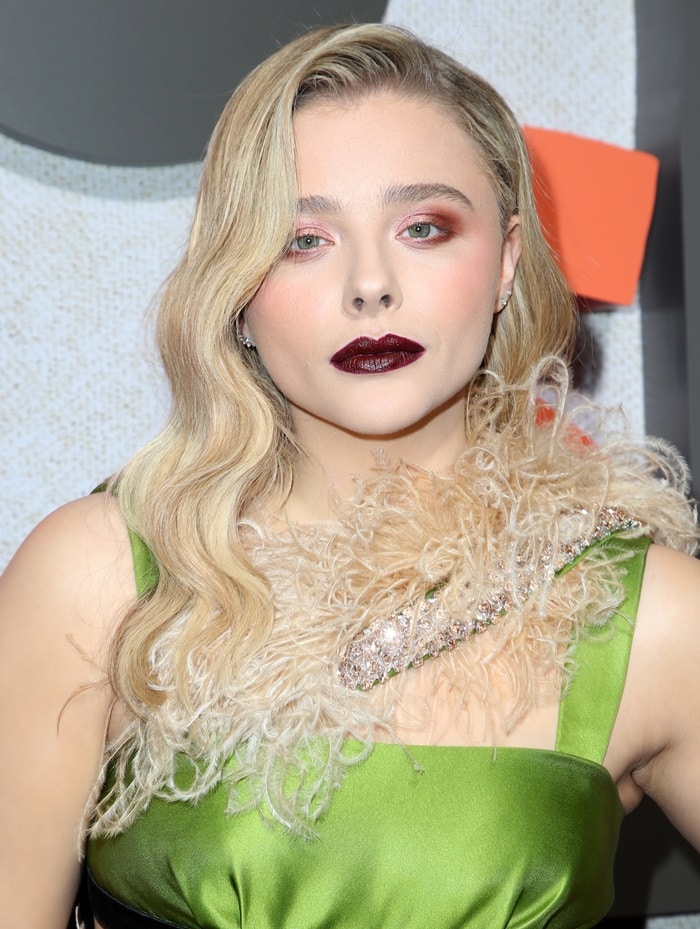 At the premiere of Suspiria, Chloë Grace Moretz embraces dramatic glamour with deep burgundy lipstick, shimmering eyeshadow, and Old Hollywood-inspired waves