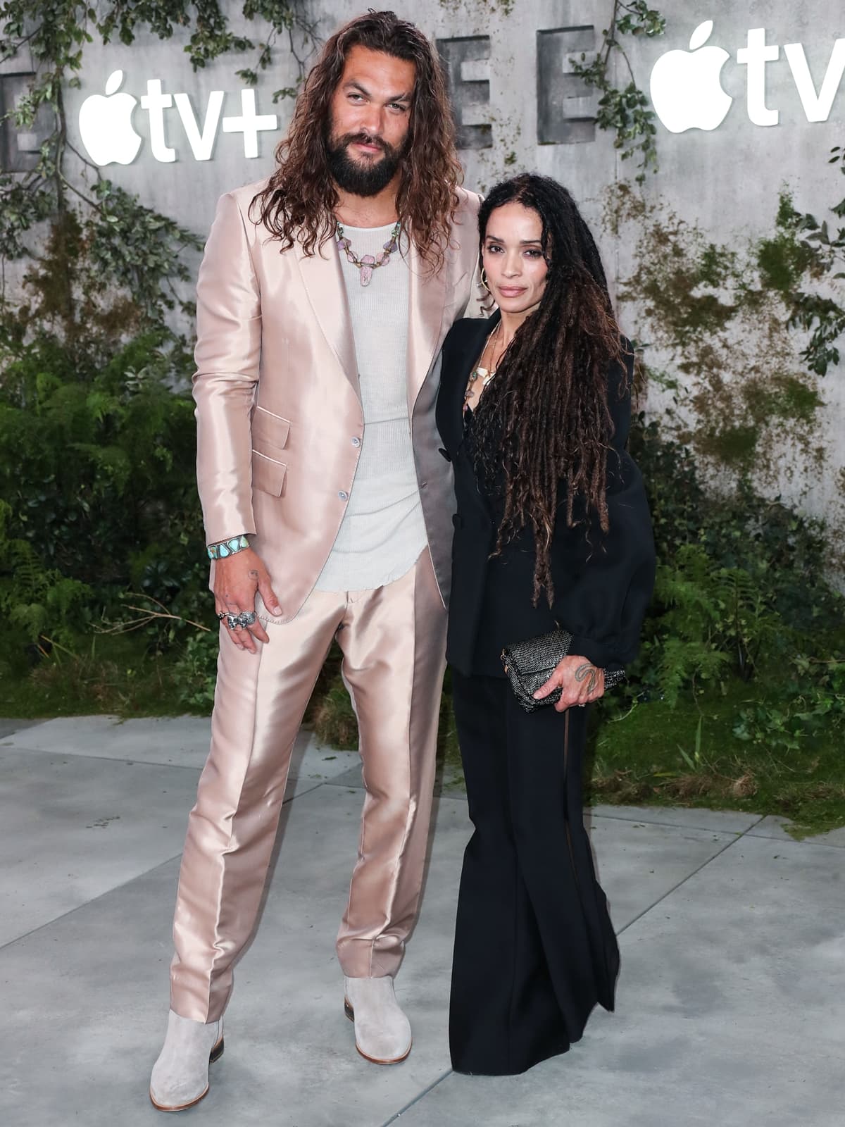 Jason Momoa and Lisa Bonet strike a stylish pose at the world premiere of Apple TV+’s See on October 21, 2019, with Momoa in a blush satin suit and suede boots, while Bonet keeps it elegant in a sleek black ensemble and platform heels