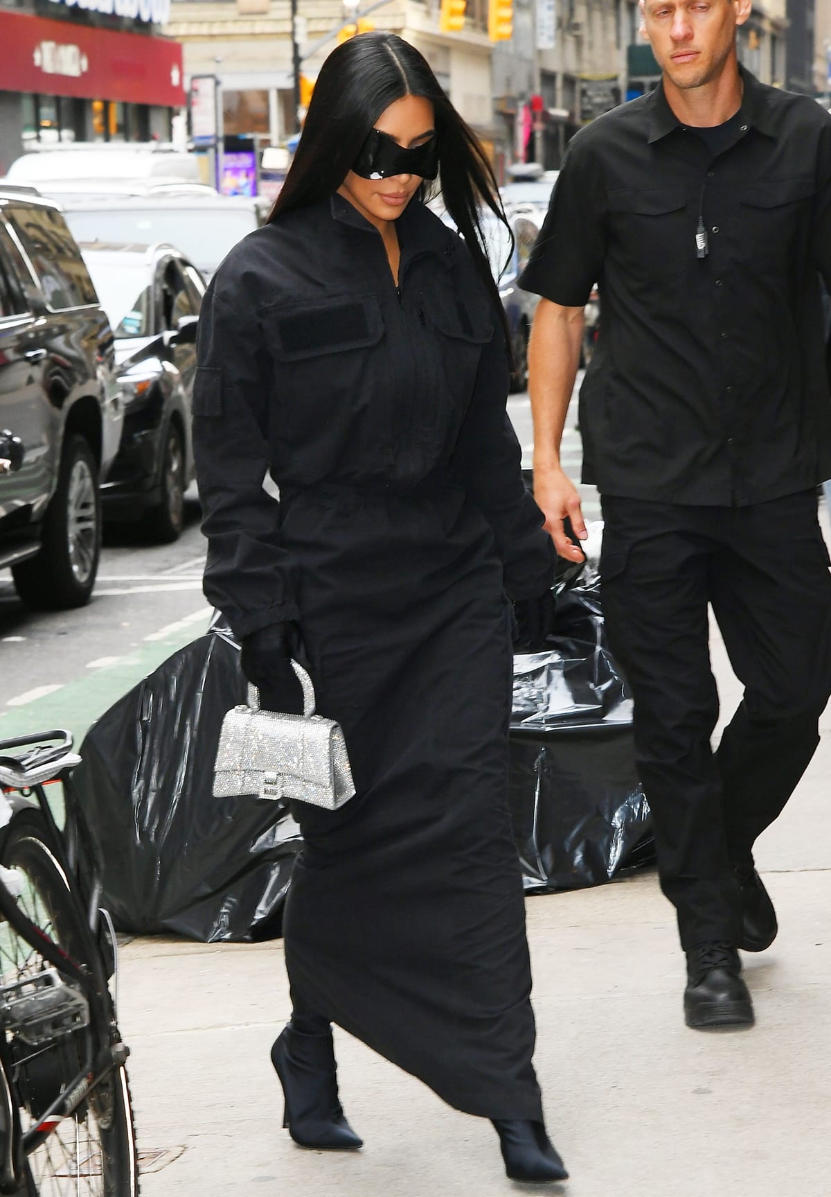 Kim Kardashian embraces Balenciaga’s dystopian aesthetic in a structured black twill gown paired with sharp Knife ankle boots, futuristic visor sunglasses, gloves, and a crystal-covered Hourglass bag while stepping out in New York City on November 2, 2021