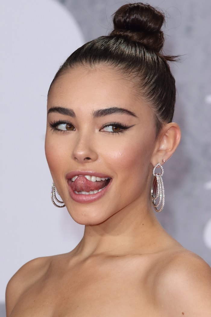 Madison Beer playfully sticks out her tongue while showing off sleek hair in a top knot and her sharp winged eyeliner at the BRIT Awards