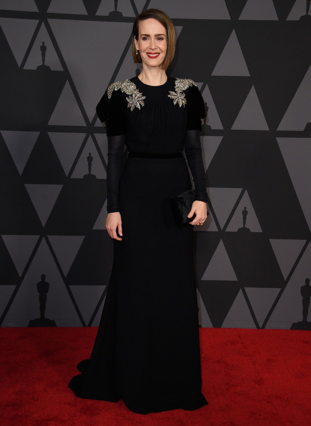 Attending the 9th Annual Governors Awards on November 11, 2017, Sarah Paulson embraced gothic glamour in a bold-shouldered, jewel-embellished Miu Miu gown, styled with a deep oxblood lip and a black Tyler Ellis clutch