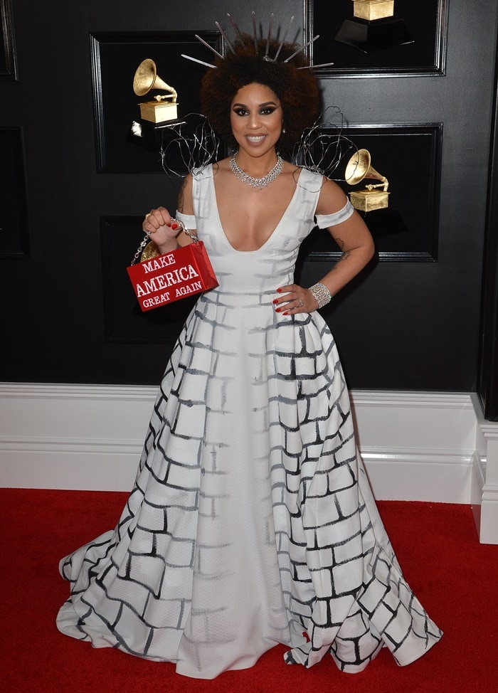 Joy Villa turned the 2019 Grammy Awards red carpet into a political fashion spectacle in a custom Desi Designs Couture gown painted with wall-inspired brick graphics and paired with a metallic red “Make America Great Again” handbag