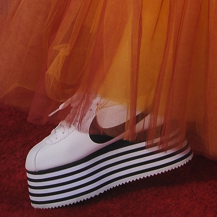 A close-up of Poppy’s bold footwear choice—a pair of Comme des Garçons x Nike Cortez platform sneakers featuring striking black-and-white striped soles that added major height and drama to her red carpet look