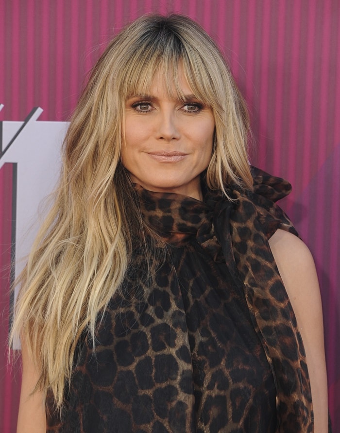 A close-up highlights her glowing neutral makeup and the dramatic bow detail that anchors the neckline of her sheer leopard-print dress
