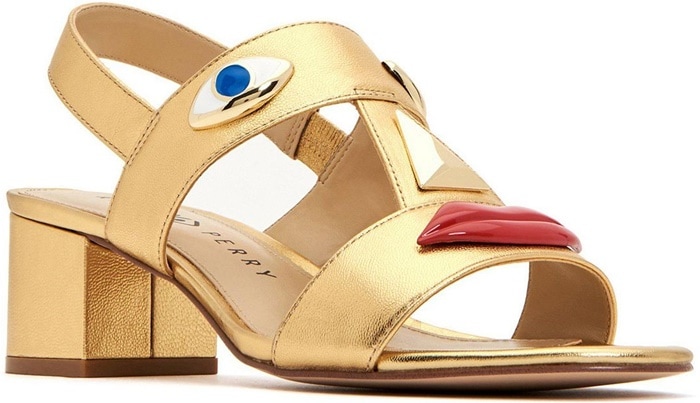The gold Ora Face block-heel sandal incorporates the collection's signature facial features across its metallic T-strap design