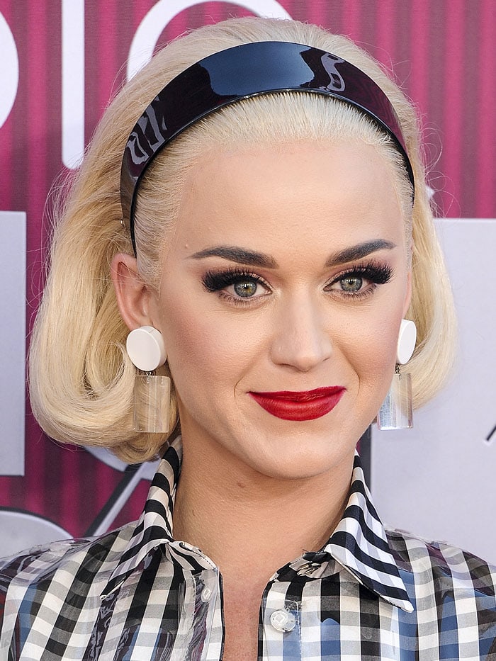 Katy Perry wearing a platinum-blonde lace-front wig, a shiny, black headband, and vintage circle lucite earrings