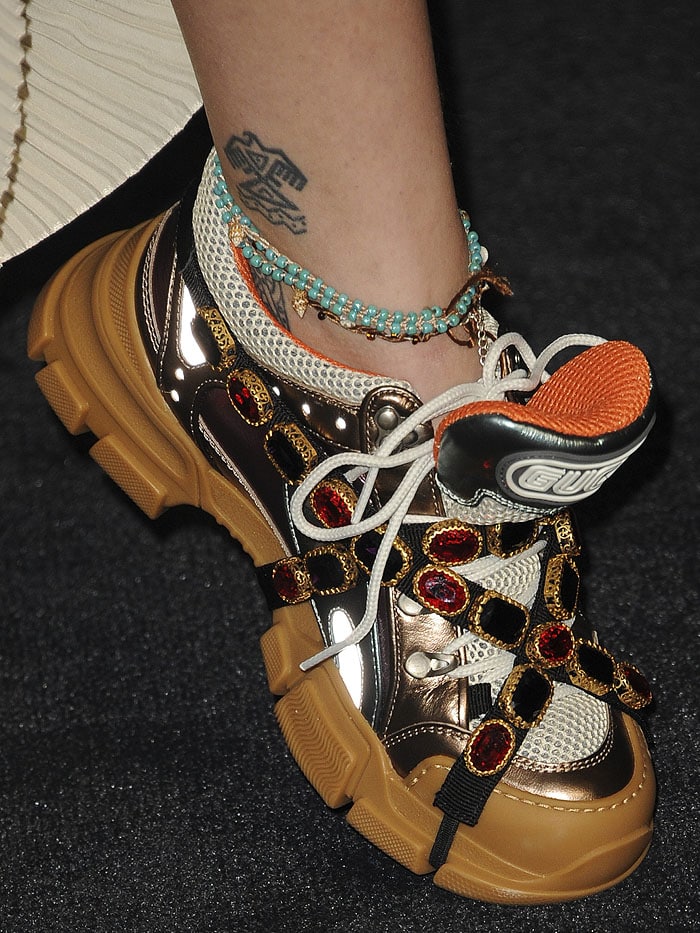 Close-up of Paris Jackson’s Gucci Flashtrek sneakers, highlighting the crystal-wrapped straps, metallic leather panels, and chunky hiking-boot sole, paired with her tribal eagle ankle tattoo for a distinctly bohemian finish
