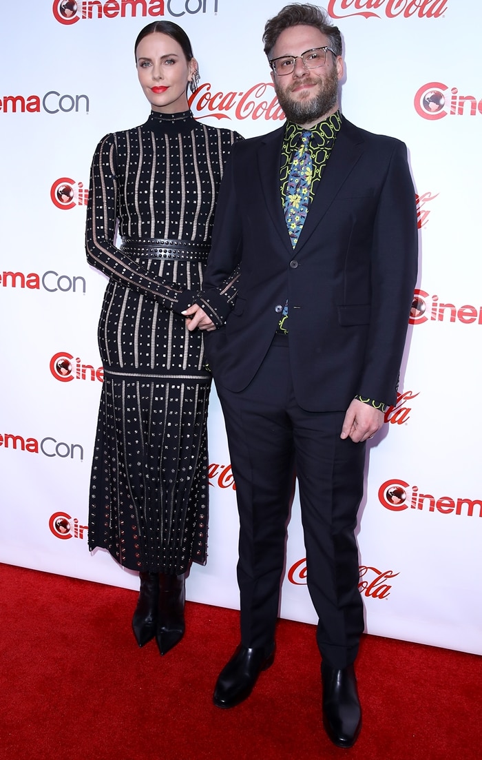 Charlize Theron poses with Seth Rogen at CinemaCon 2019, her studded black look finished with sleek pointed-toe boots that visually elevate her statuesque frame on the red carpet