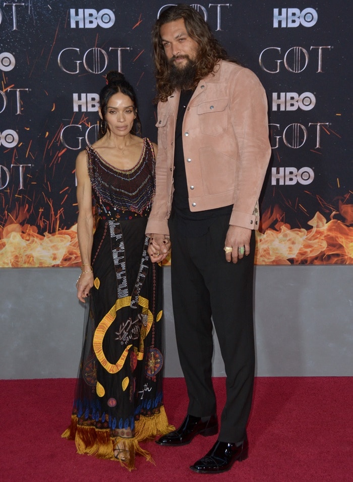 Lisa Bonet stuns in a Motherpeace Tarot-inspired vintage Dior gown with intricate fringe, while Jason Momoa complements her look in a peach suede Tom Ford jacket, black Valentino shirt, and glossy Fendi shoes