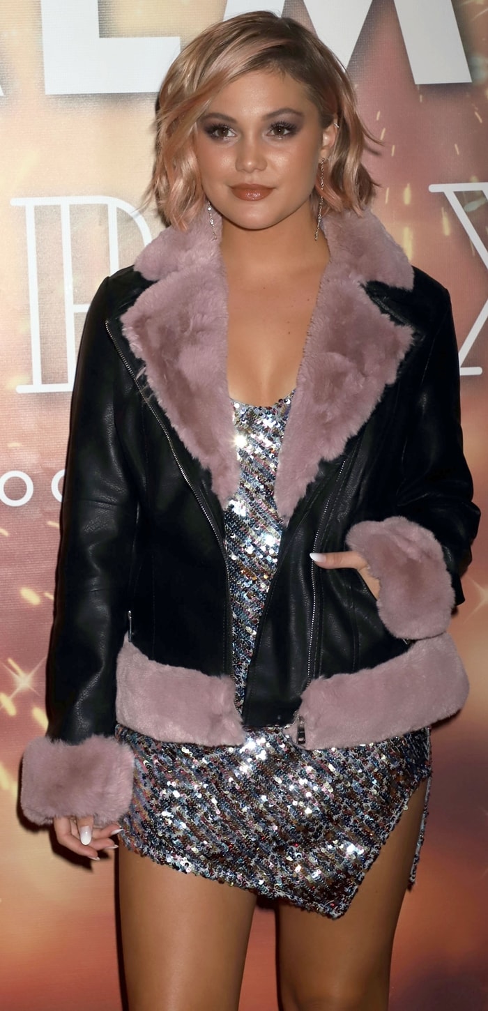 Olivia Holt layered a black Coalition LA shearling-trim jacket over her shimmering For Love Lemons mini dress, adding a softer contrast to the high-shine New Year’s Eve look