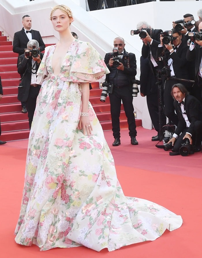 Elle Fanning glides up the Cannes red carpet in a sweeping Valentino Spring 2019 Haute Couture gown, its soft floral jacquard and extended train creating a romantic contrast against the festival’s iconic scarlet steps