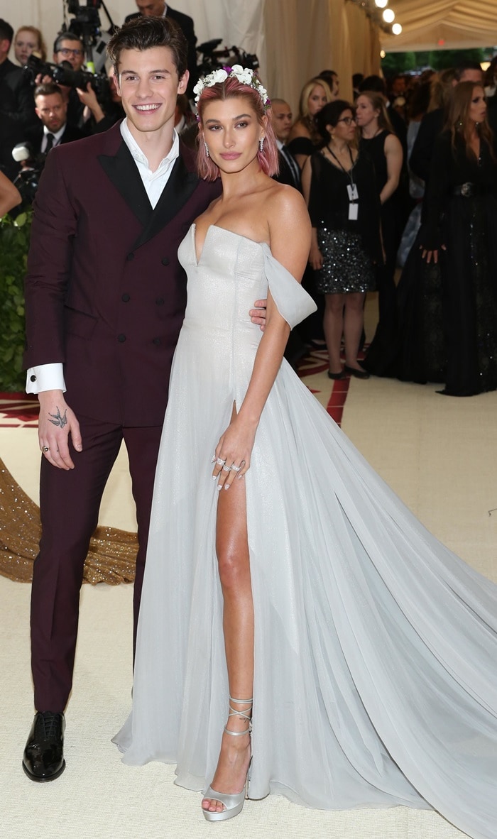At the 2018 Met Gala, Hailey Baldwin attended alongside Shawn Mendes in a romantic gray Tommy Hilfiger gown styled with metallic lace-up heels and floral hair accessories, reflecting the softer, princess-inspired aesthetic she favored before her dramatic Alexander Wang transformation a year later
