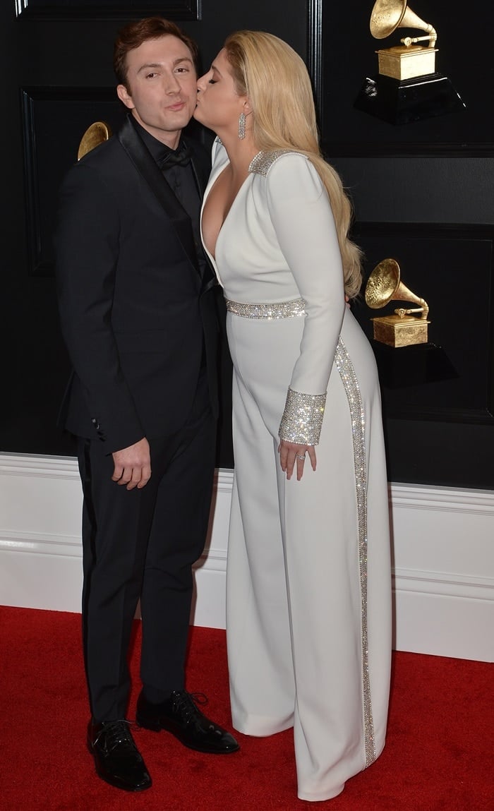Meghan Trainor kisses husband Daryl Sabara on the 2019 Grammys red carpet while wearing a crystal-trimmed white Christian Siriano pantsuit