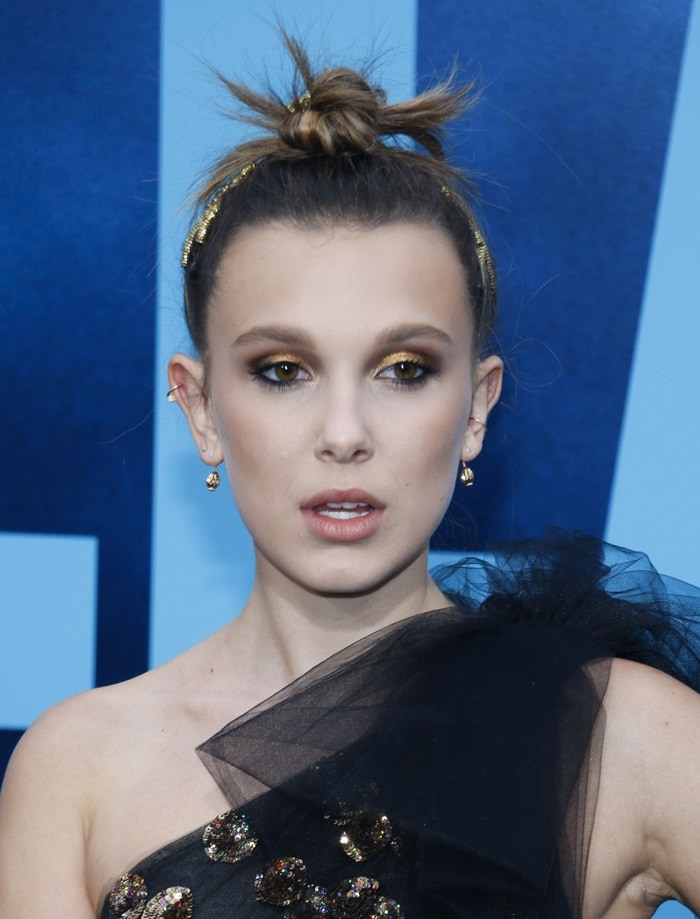 Millie Bobby Brown goes glam with golden eye makeup, a sleek topknot, and delicate Cartier jewels to complement her dramatic Oscar de la Renta gown